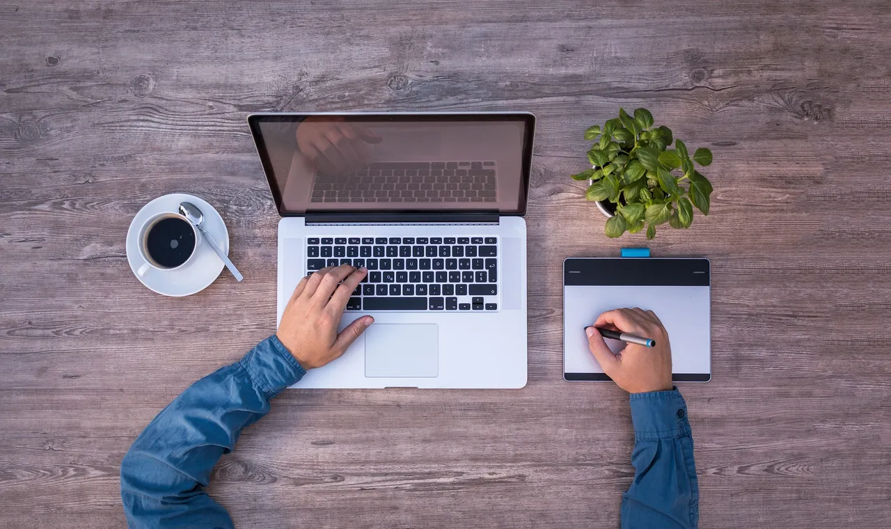 Overhead view of a laptop, coffee and notebook on a wooden desk
